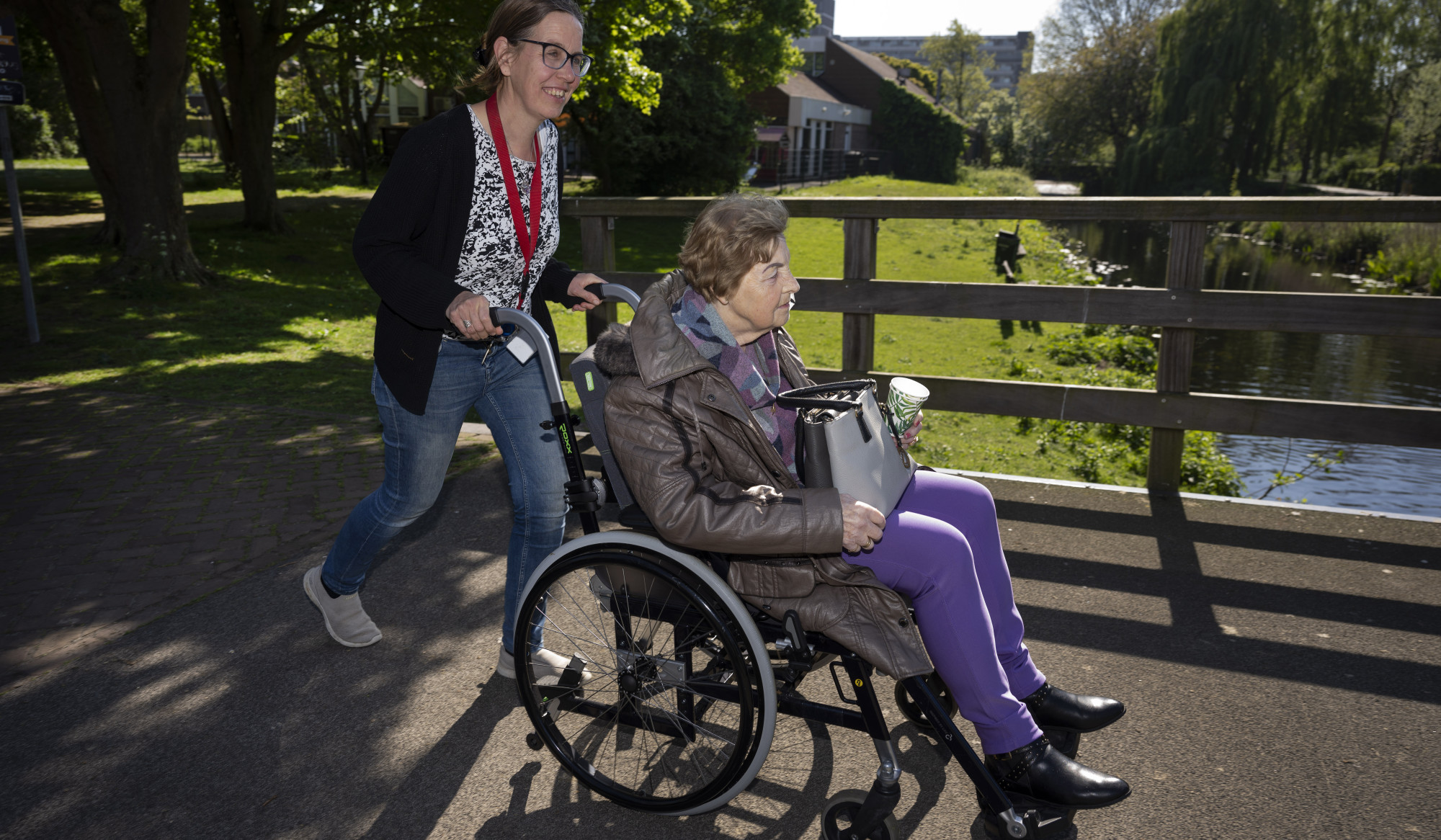 Persoon duwt dame in rolstoel over bruggetje